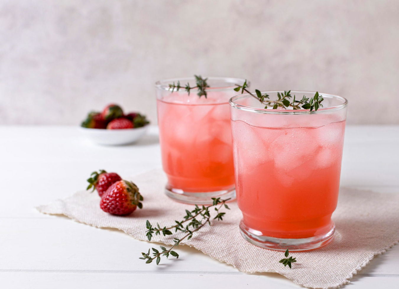 Deux verres de boisson rosée glacée, garnis de thym, avec des fraises